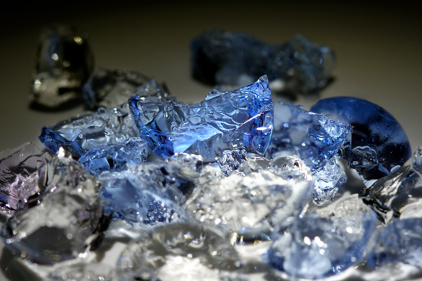 A close-up view of scattered translucent fragments fills the frame—irregular pieces of glass or ice in shades of clear and cool blue. The shards catch and refract the light, creating bright highlights and soft internal reflections. Some pieces are sharply angular, others rounded, all piled together in a way that feels both chaotic and carefully observed. The background is softly blurred, drawing attention to the crisp textures and luminous edges in the foreground.
The image feels delicate yet tense. The shimmering blues and sparkling light give it a sense of beauty and fragility, but the jagged edges suggest something broken or disrupted. Emotionally, it evokes a mix of fascination and unease—like admiring something exquisite that could also cut if touched. There’s a quiet intensity in the stillness, as if capturing the aftermath of a moment of fracture, where beauty persists within damage.