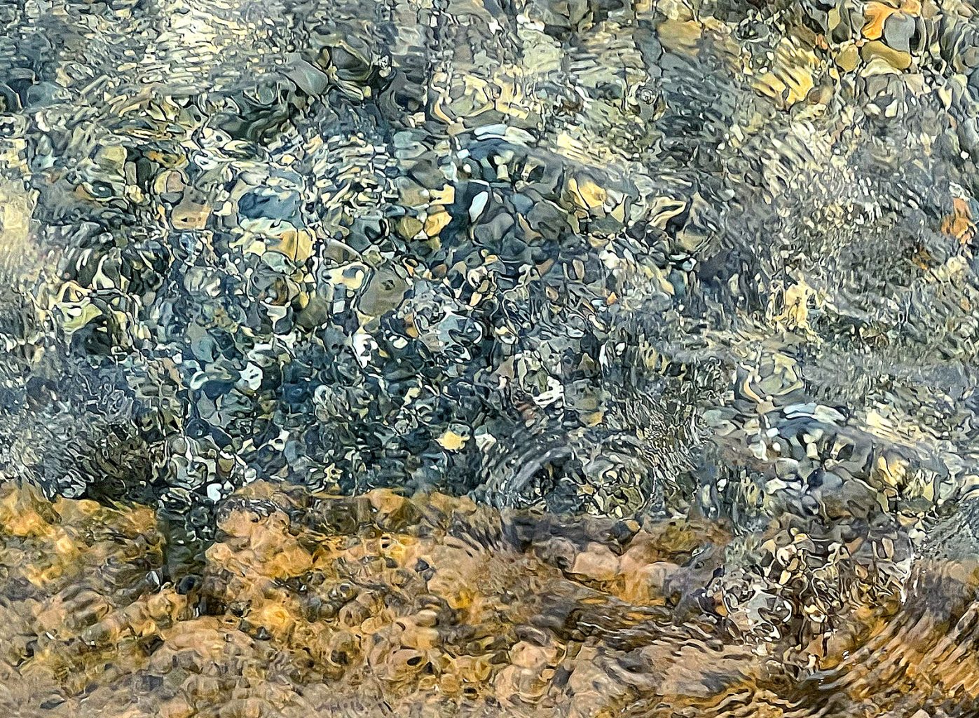 Abstrakte Wasseroberfläche über hellen Steinen: Dunkle, gebrochene Linien, spiegelnde Flächen und helle Lichtreflexe bilden eine flüchtige Komposition. Das Bild wirkt lebendig, verspielt und still verzaubernd – wie ein ungemaltes Kunstwerk, das sich im nächsten Augenblick verwandelt.
Abstract water surface above pale stones: dark broken lines, mirrored shapes and bright reflections form a fleeting composition. The image feels alive, playful and quietly enchanting, like an unpainted work of art already changing into something new in the very next moment.