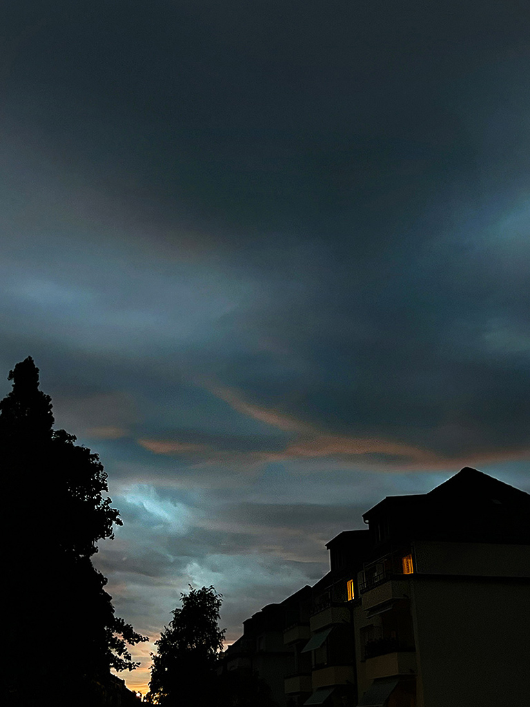 Dunkler Abendhimmel mit schweren Wolken über der Silhouette eines Hauses; zwei Fenster leuchten warm, am Horizont glimmt Orange. Das Bild erzählt von Geborgenheit und Scheinsicherheit – und vom leisen Wagnis, sich dem Ungewissen zu öffnen.
Dark evening sky with heavy clouds above the silhouette of a house; two windows glow warmly, while orange lingers on the horizon. The image evokes shelter and false safety – and the quiet courage it takes to open oneself to the unknown.